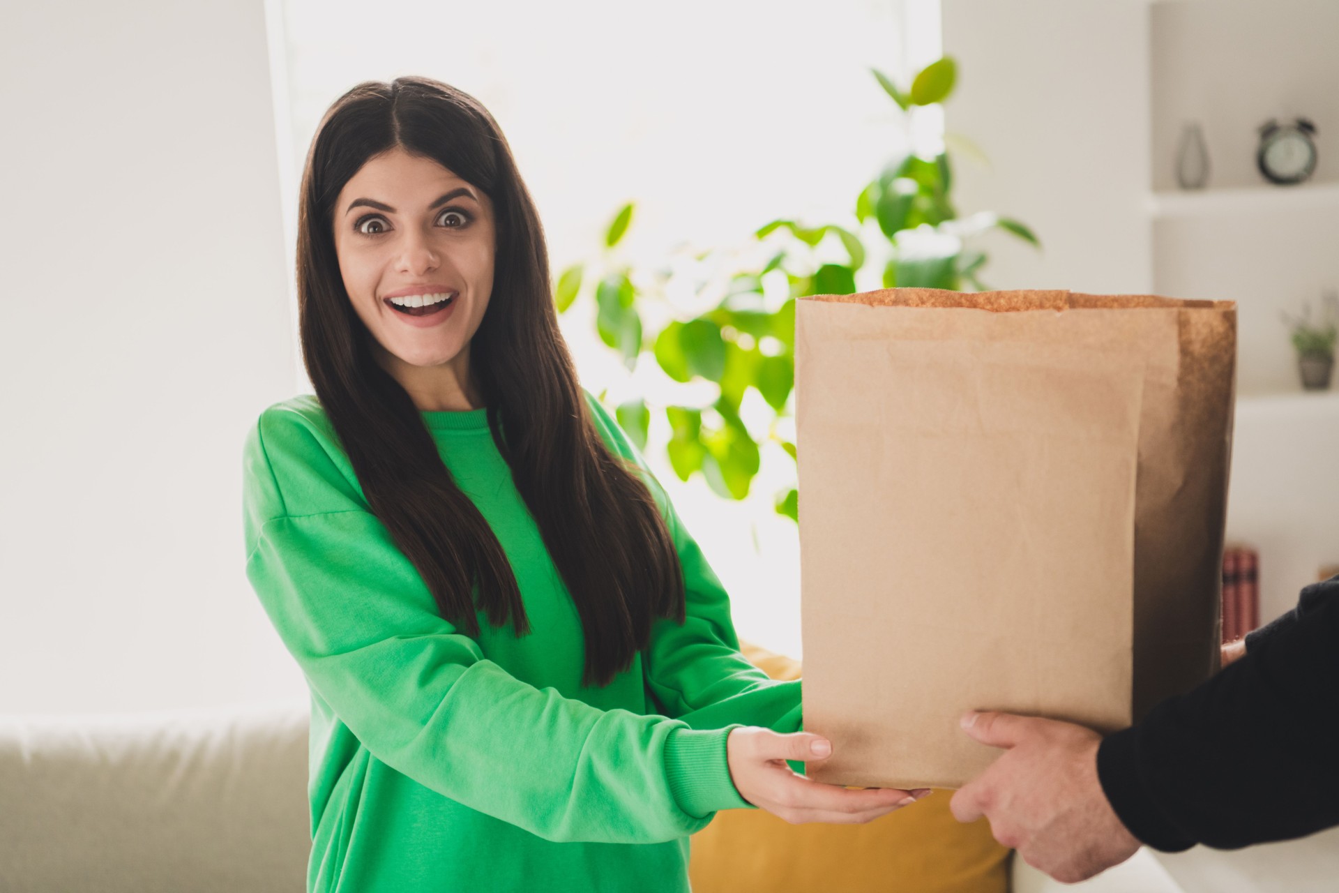 Young woman in casual outfit receiving a package indoors with excitement and joy